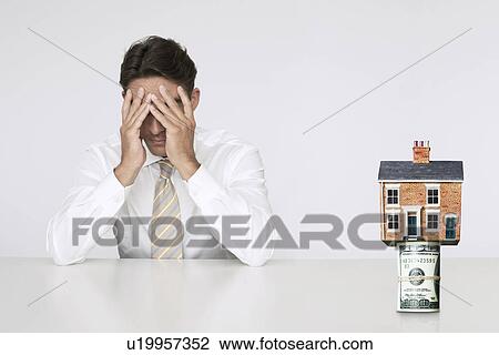 Worried businessman at table with house on top of bills representing increasing real estate rates View Large Photo Image Stock Image - Worried businessman at table with house on top of bills representing increasing real estate rates. Fotosearch
