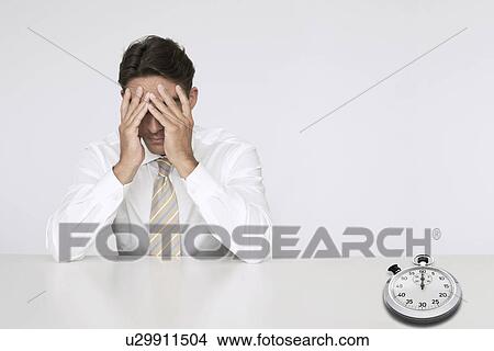 Worried businessman at table with stopwatch representing loss of time View Large Photo Image Picture - Worried businessman at table with stopwatch representing loss of time. Fotosearch
