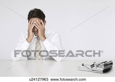 Stock Image - Worried businessman at table with wad of cash in mouse trap representing financial difficulties. Fotosearch