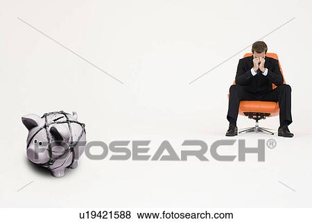 Worried businessman on chair and piggybank tied with rope representing financial difficulties View Large Photo Image Stock Photo - Worried businessman on chair and piggybank tied with rope representing financial difficulties. Fotosearch