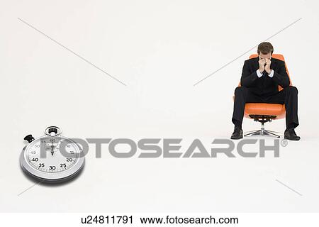 Stock Image - Worried businessman sitting on chair with stopwatch representing loss of time. Fotosearch