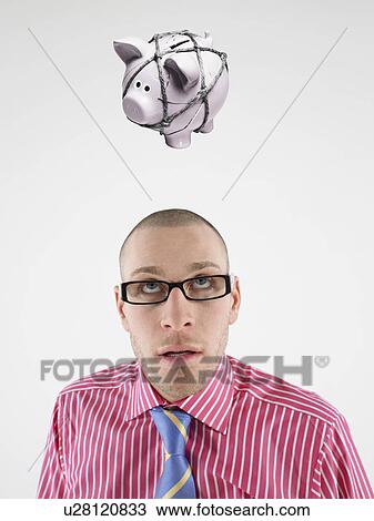 Young businessman looking up at piggy bank tied with rope representing trapped finances View Large Photo Image Stock Image - Young businessman looking up at piggy bank tied with rope representing trapped finances. Fotosearch