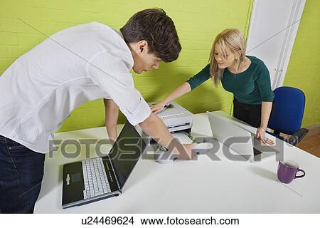 Young businesspeople setting up printer with laptops at desk View Large Photo Image Picture - Young businesspeople setting up printer with laptops at desk. Fotosearch