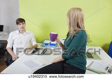 Young businesswoman conversing with male coworker in office break View Large Photo Image Stock Photography - Young businesswoman conversing with male coworker in office break. Fotosearch