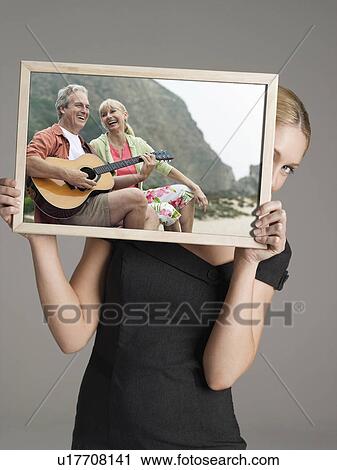 Young businesswoman peeking from behind photograph of happy couple with guitar on vacation against gray background View Large Photo Image Stock Image - Young businesswoman peeking from behind photograph of happy couple with guitar on vacation against gray background. Fotosearch