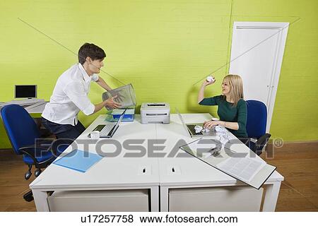 Young businesswoman throwing paper ball at male colleague holding waste bin View Large Photo Image Stock Photo - Young businesswoman throwing paper ball at male colleague holding waste bin. Fotosearch