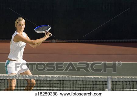 Stock Photo - Young female tennis player swinging racket at court. Fotosearch