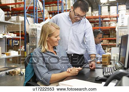Stock Image - Business Colleagues Working At Desk In Warehouse. Fotosearch
