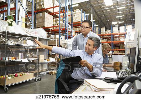 Stock Photograph - Business Colleagues Working At Desk In Warehouse. Fotosearch