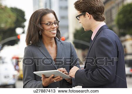 Stock Image - Businessman And Businesswoman Using Digital Tablet Outside . Fotosearch