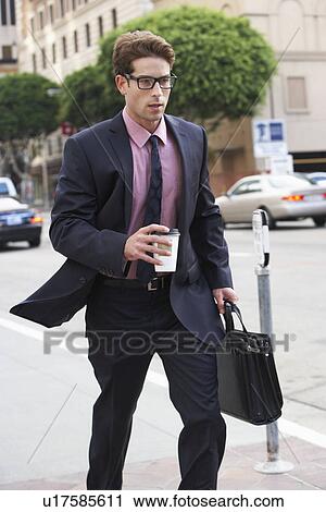 Stock Image - Businessman Hurrying Along Street Holding Takeaway Coffee. Fotosearch