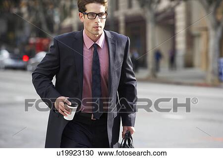 Stock Image - Businessman Hurrying Along Street Holding Takeaway Coffee. Fotosearch