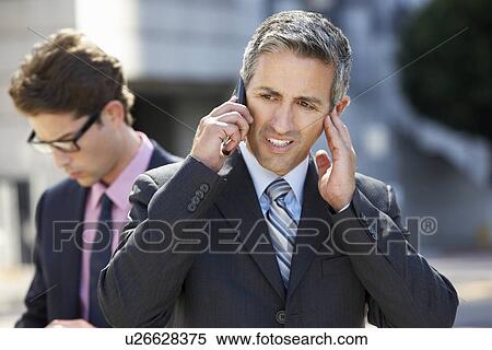 Businessman Speaking On Mobile Phone In Noisy Surroundings View Large Photo Image Stock Photography - Businessman Speaking On Mobile Phone In Noisy Surroundings. Fotosearch