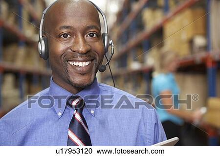 Stock Image - Businessman Using Headset In Distribution Warehouse. Fotosearch