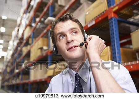 Stock Image - Businessman Using Headset In Distribution Warehouse. Fotosearch