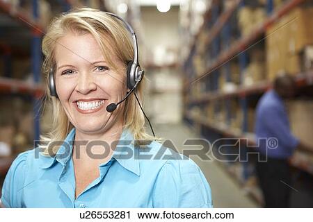 Stock Image - Businesswoman Using Headset In Distribution Warehouse. Fotosearch