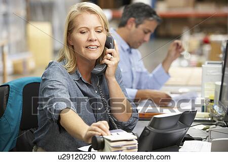 Stock Image - Businesswoman Working At Desk In Warehouse. Fotosearch