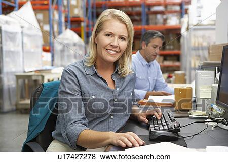 Stock Photo - Businesswoman Working At Desk In Warehouse. Fotosearch