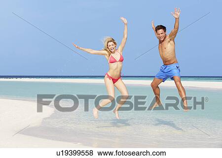 Stock Photo - Couple Jumping On Beautiful Tropical Beach . Fotosearch