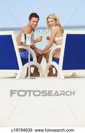 Stock Photo - Couple On Beach Relaxing In Chairs And Drinking Chapagne. Fotosearch