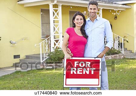 Stock Image - Couple Standing By For Rent Sign Outside Home. Fotosearch