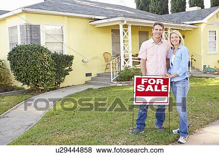 Stock Photo - Couple Standing By For Sale Sign Outside Home. Fotosearch