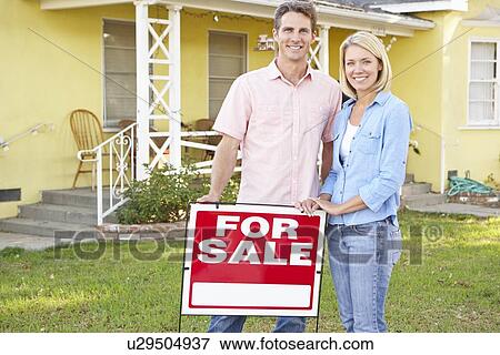 Stock Photo - Couple Standing By For Sale Sign Outside Home. Fotosearch