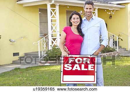 Stock Photography - Couple Standing By For Sale Sign Outside Home. Fotosearch