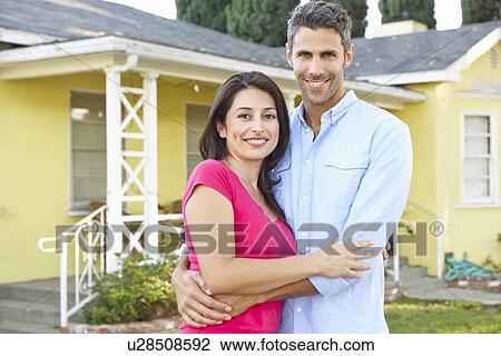 Stock Image - Couple Standing Outside Suburban Home. Fotosearch