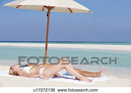 Stock Photograph - Couple Sunbathing On Beautiful Beach Holiday. Fotosearch