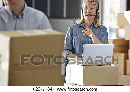Stock Photo - Female Manager Using Headset In Distribution Warehouse. Fotosearch