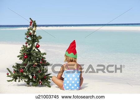 Stock Photography - Girl Sitting On Beach With Christmas Tree And Hat. Fotosearch