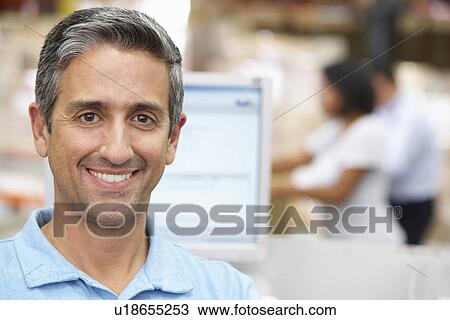 Stock Image - Man At Computer Terminal In Distribution Warehouse. Fotosearch