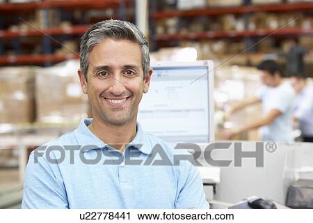 Stock Image - Man At Computer Terminal In Distribution Warehouse. Fotosearch
