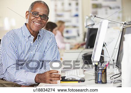Man Holding Cup Working At Desk In Busy Creative Office View Large Photo Image Picture - Man Holding Cup Working At Desk In Busy Creative Office. Fotosearch
