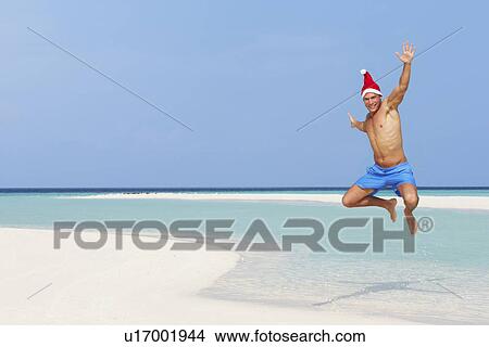 Picture - Man Jumping On Beach Wearing Santa Hat. Fotosearch