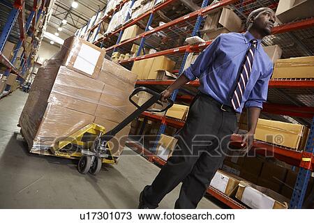 Stock Image - Man Pulling Pallet In Warehouse. Fotosearch