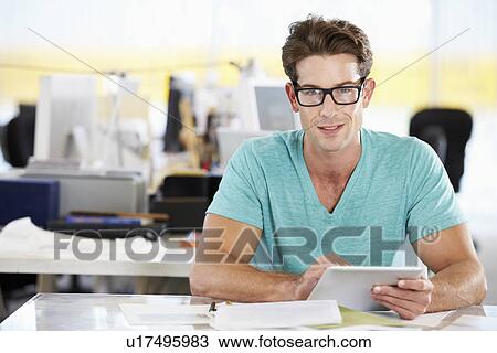 Stock Image - Man Using Digital Tablet In Busy Creative Office. Fotosearch