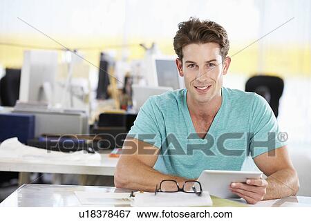 Stock Photo - Man Using Digital Tablet In Busy Creative Office. Fotosearch