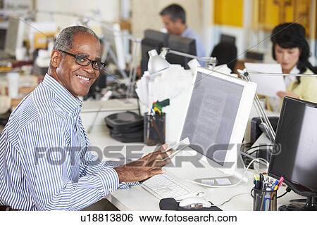 Stock Photograph - Man Using Digital Tablet In Busy Creative Office. Fotosearch