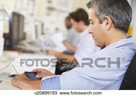 Man Using Mobile Phone At Desk In Busy Creative Office View Large Photo Image Stock Image - Man Using Mobile Phone At Desk In Busy Creative Office. Fotosearch