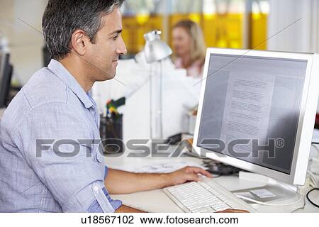 Stock Image - Man Working At Desk In Busy Creative Office. Fotosearch