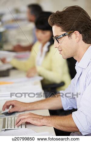 Stock Image - Man Working At Desk In Busy Creative Office. Fotosearch