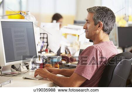 Man Working At Desk In Busy Creative Office View Large Photo Image Stock Photo - Man Working At Desk In Busy Creative Office. Fotosearch