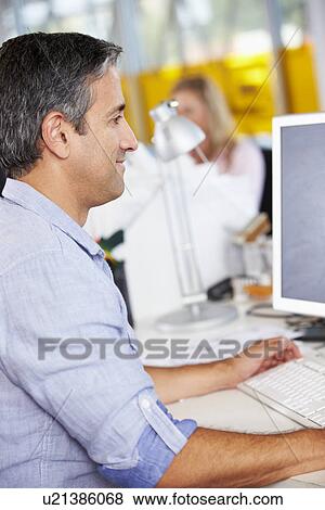 Man Working At Desk In Busy Creative Office View Large Photo Image Stock Photo - Man Working At Desk In Busy Creative Office. Fotosearch