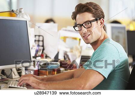 Stock Photo - Man Working At Desk In Busy Creative Office. Fotosearch