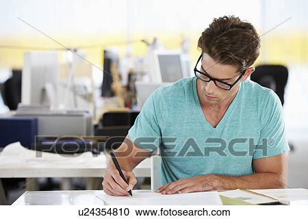 Stock Image - Man Writing At Desk In Busy Creative Office. Fotosearch