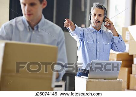 Stock Photograph - Manager Using Headset In Distribution Warehouse. Fotosearch