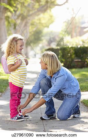 Stock Image - Mother Helping Daughter Tie Shoe Laces On Walk To School . Fotosearch