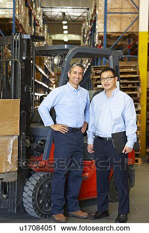 Stock Image - Portrait Of Businessmen With Fork Lift Truck In Warehouse. Fotosearch